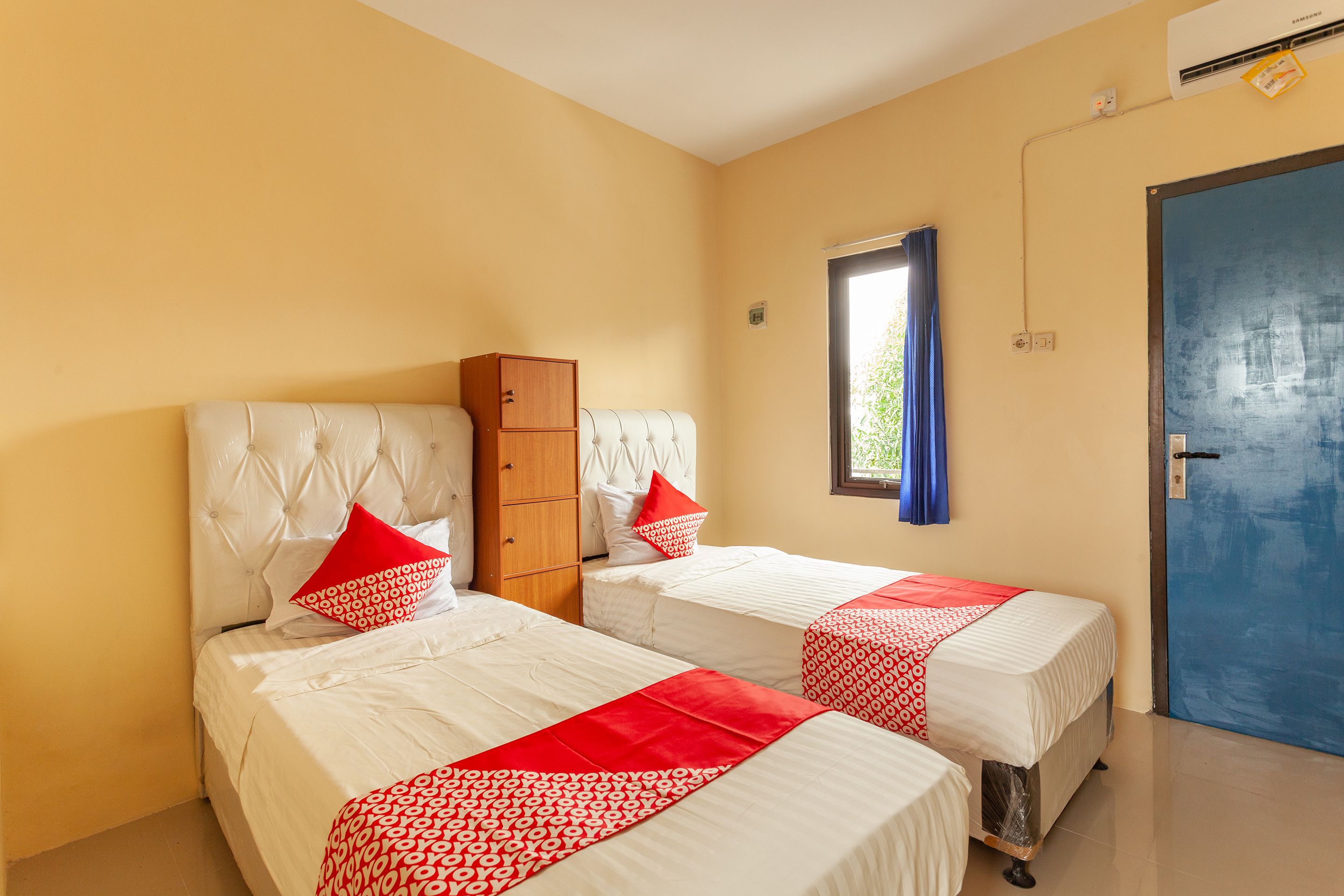 A hotel room with two beds, a wardrobe, a window with a view, and a blue door.