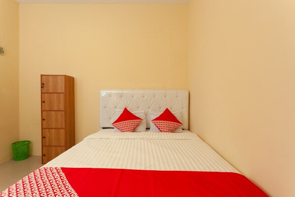 A bedroom with a bed, a wooden wardrobe, and a green trash bin. - OYO 588 Richmond Guest House (West Cirebon)