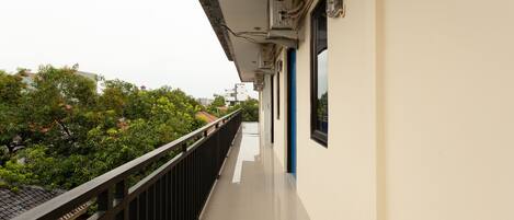 A corridor with a black railing, a tiled floor, and air conditioning units on the wall.