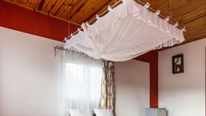 Een slaapkamer met een houten plafond, een bed met wit beddengoed, een nachtkastje met een lamp.
