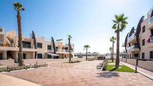 A modern building complex with multiple balconies, palm trees, and a paved courtyard.