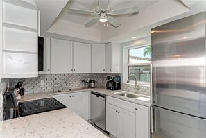 A modern kitchen with white cabinets, a stainless steel refrigerator, a coffee maker, and a window with a view of palm trees.