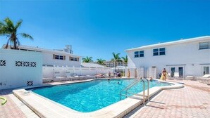 A swimming pool with a tiled deck, surrounded by white buildings and palm trees. - Crystal Sands Villa 12 - Private Beach (Sarasota)