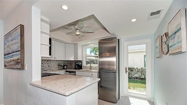 A modern kitchen with white cabinets, a stainless steel refrigerator, and a large island. - Crystal Sands Villa 12 - Private Beach (Sarasota)