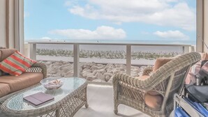 Ein Balkon mit Korbmöbeln, einem Glastisch und Blick auf den Strand.