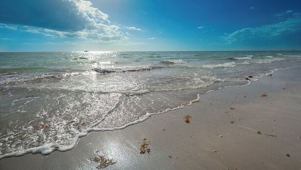 Ein Strand mit Wellen, einem klaren Himmel und einem Boot in der Ferne.