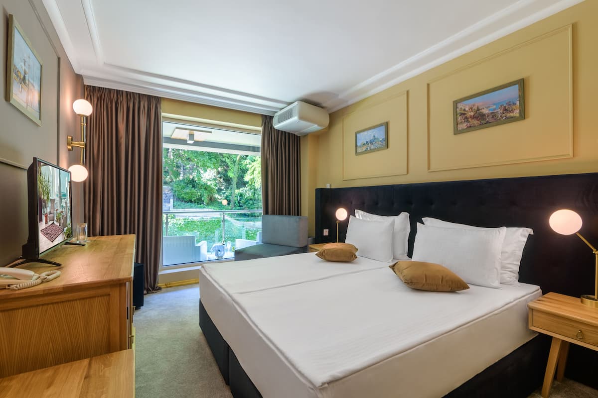 A hotel room with a large bed, a desk with a telephone, a chair, and a window with curtains.