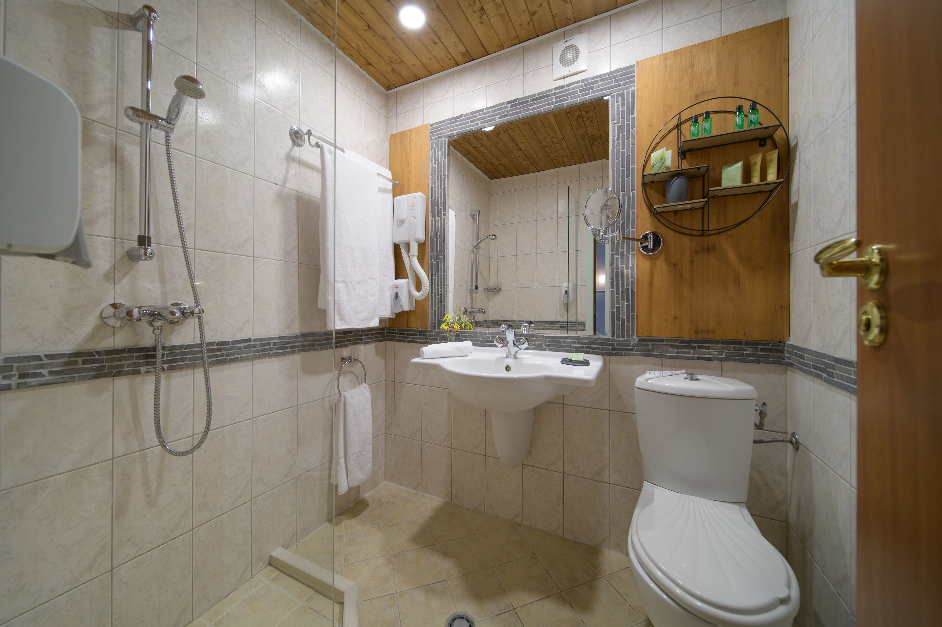 A bathroom with a shower, sink, toilet, and a wooden vanity with a mirror.