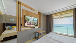 A hotel room with a large bed, a desk, a TV mounted on the wall, and a view of the sea. - Marina Sunny Day Resort (Varna)