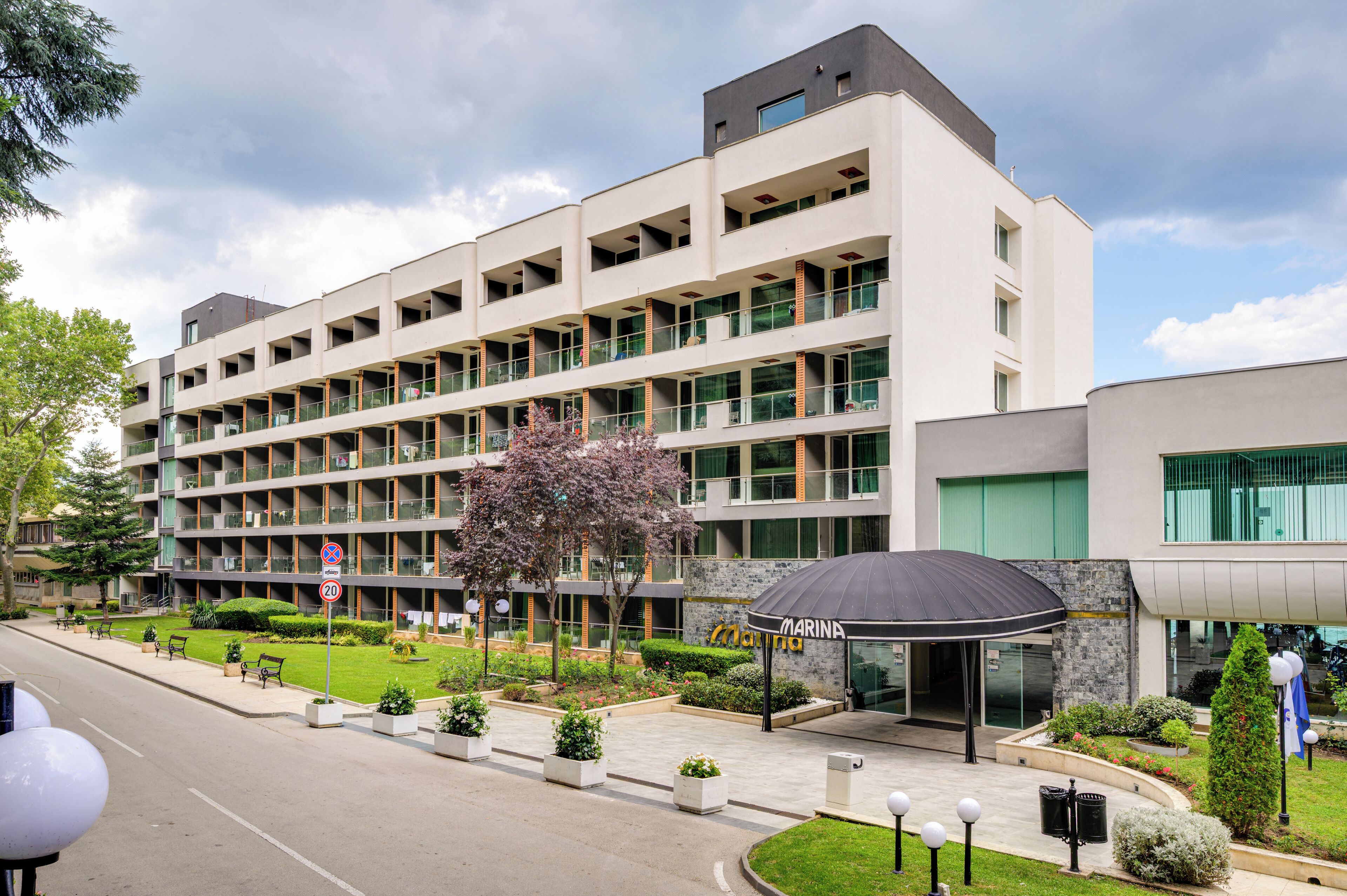 A multi-story hotel with a modern design, featuring balconies, a landscaped garden, and a covered entrance.