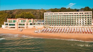A beachfront hotel with multiple floors, a beach with rows of umbrellas, and a hillside in the background. - Marina Sunny Day Resort (Varna)