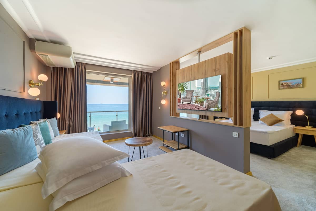 A hotel room with a large bed, a desk, a chair, a TV, and a view of the sea.