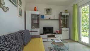 A living room with a sofa, TV, glass coffee table, and shelves with decorative items. - Flower House (Kastela)