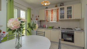 A kitchen with a white table, a vase with flowers, and a stove. - Flower House (Kastela)