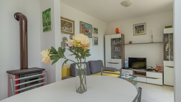 A modern living room with a round table, a TV, and a bookshelf. - Flower House (Kastela)