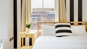 Ett hotellrum med en säng, ett nattduksbord, ett fönster med gardiner och utsikt över byggnader utanför.