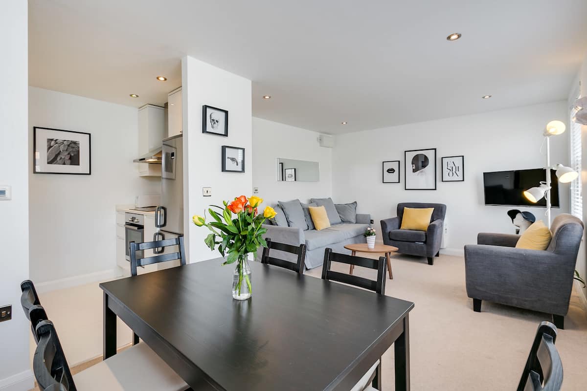 A modern living room with a dining table, grey sofas, and a TV.