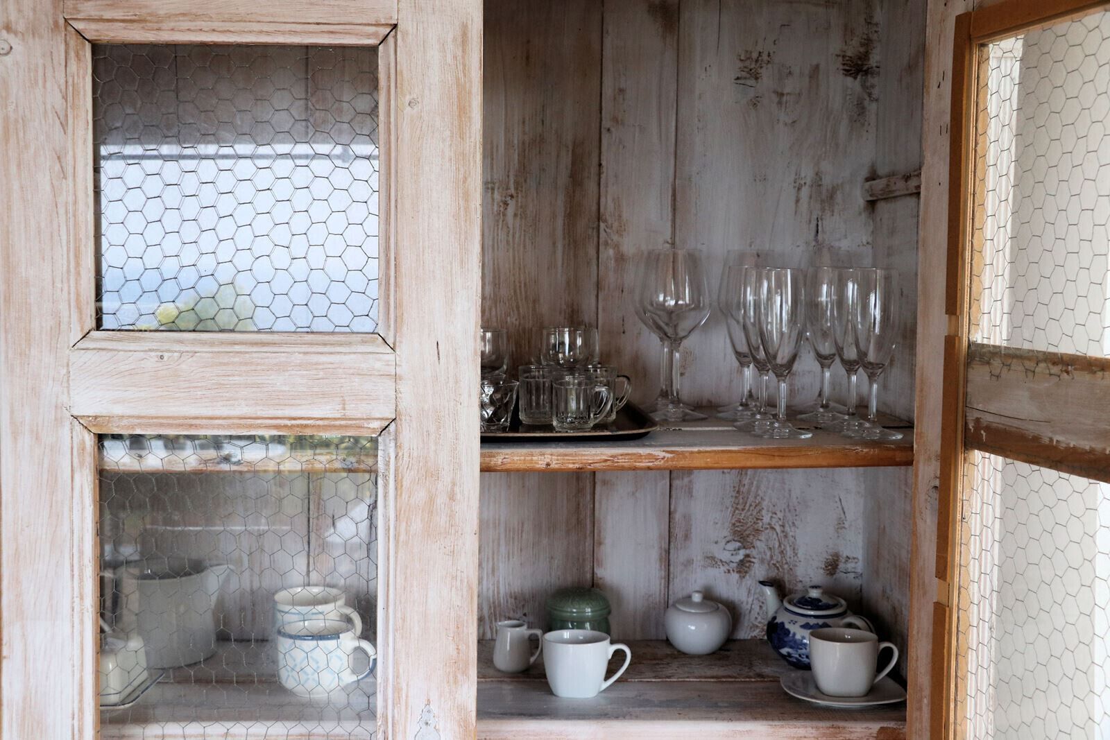 Un buffet en bois rustique, doté de portes en verre, renfermant divers objets en verre et en céramique.