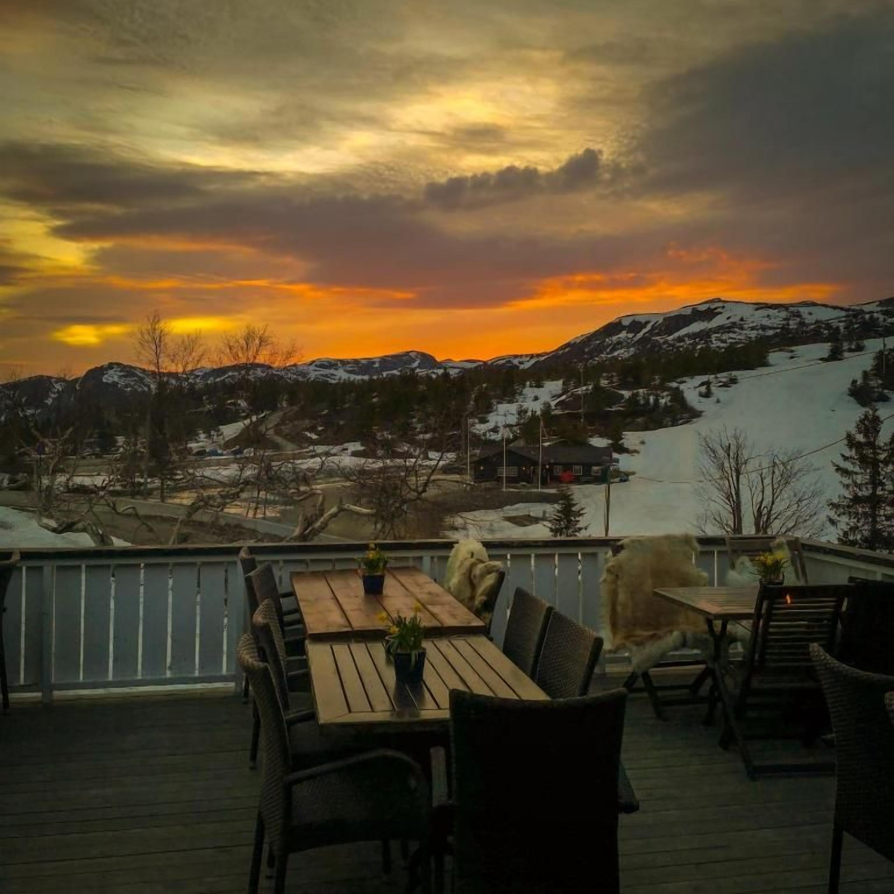 A deck with outdoor seating and a view of a snowy landscape during sunset.
