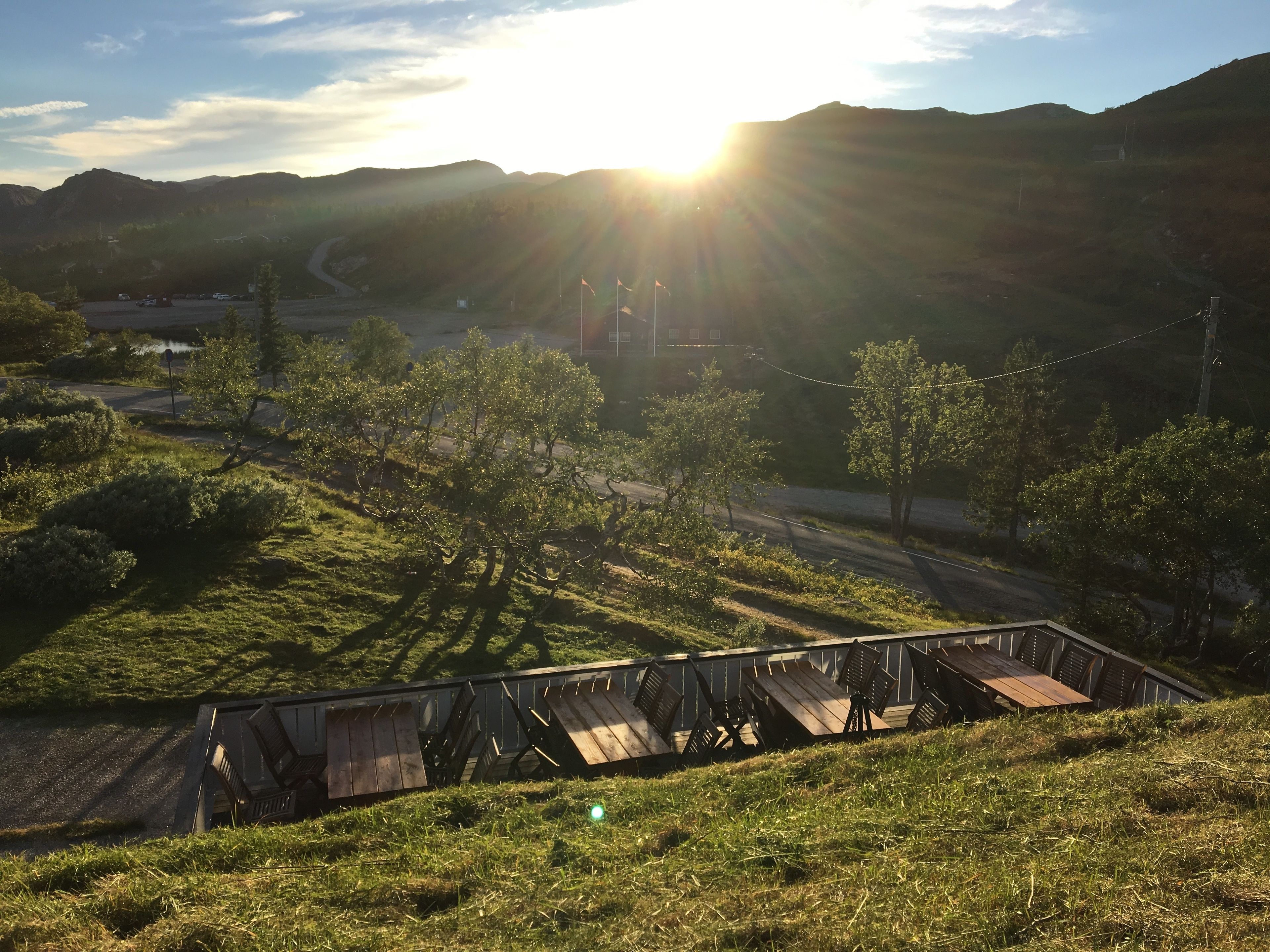 Ländliche Landschaft mit einer Holzhütte an einem Hügel, einer Straße und fernen Hügeln.