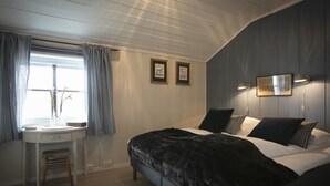 Un dormitorio con cama, mesitas de noche, escritorio y ventana con cortinas.