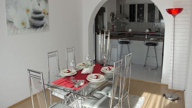 A dining area with a glass table, metal chairs, and a red tablecloth. There is a kitchen visible through an archway in the background. - Apartment Marija (Kastela)