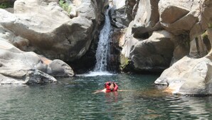 Una persona con chaleco salvavidas rojo nadando en un cuerpo de agua natural rodeado de grandes rocas.