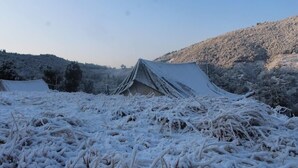 Una estructura tipo tienda con techo nevado, rodeada de un paisaje y colinas cubiertas de nieve.