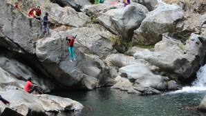 Un paisaje rocoso con una cascada pequeña y personas sentadas sobre las rocas.