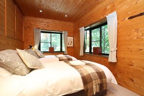 Un dormitorio de cabaña de madera con dos camas, ventanas amplias y una lámpara en el techo.