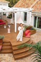Een overdekt buitengebied met een houten trap, een witte pergola en een rode bank.