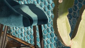 Una silla con un cojín azul, un cactus y una pared de azulejos con un diseño geométrico.