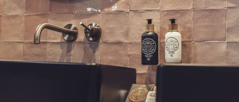 Une salle de bain avec un lavabo noir, un miroir rond et deux flacons de savon pour les mains fixés au mur.