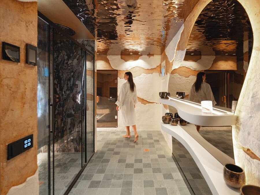 A modern bathroom with a marble floor, a glass shower enclosure, and a large mirror above the sink.