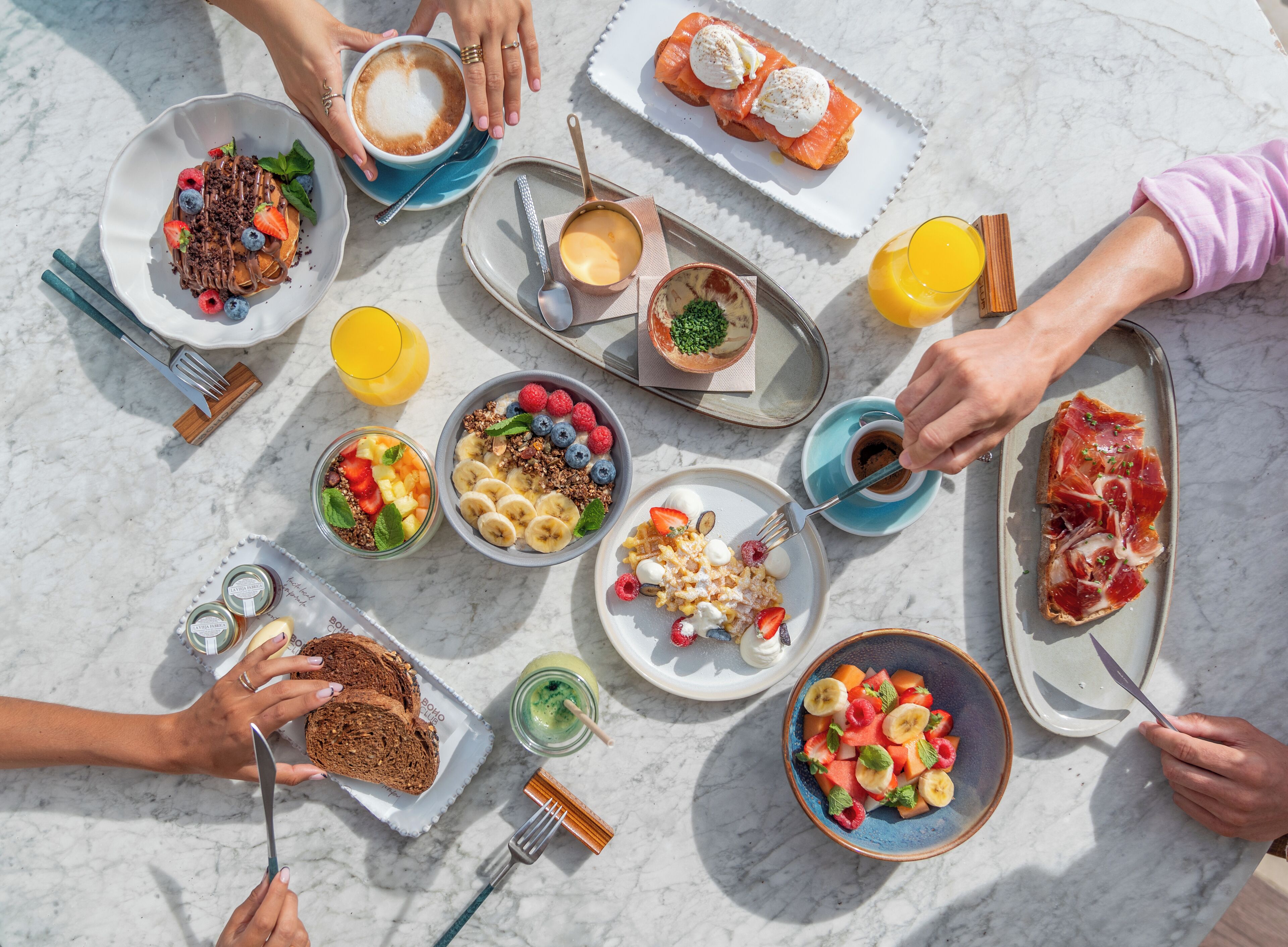 A breakfast spread with various dishes and drinks on a marble table.