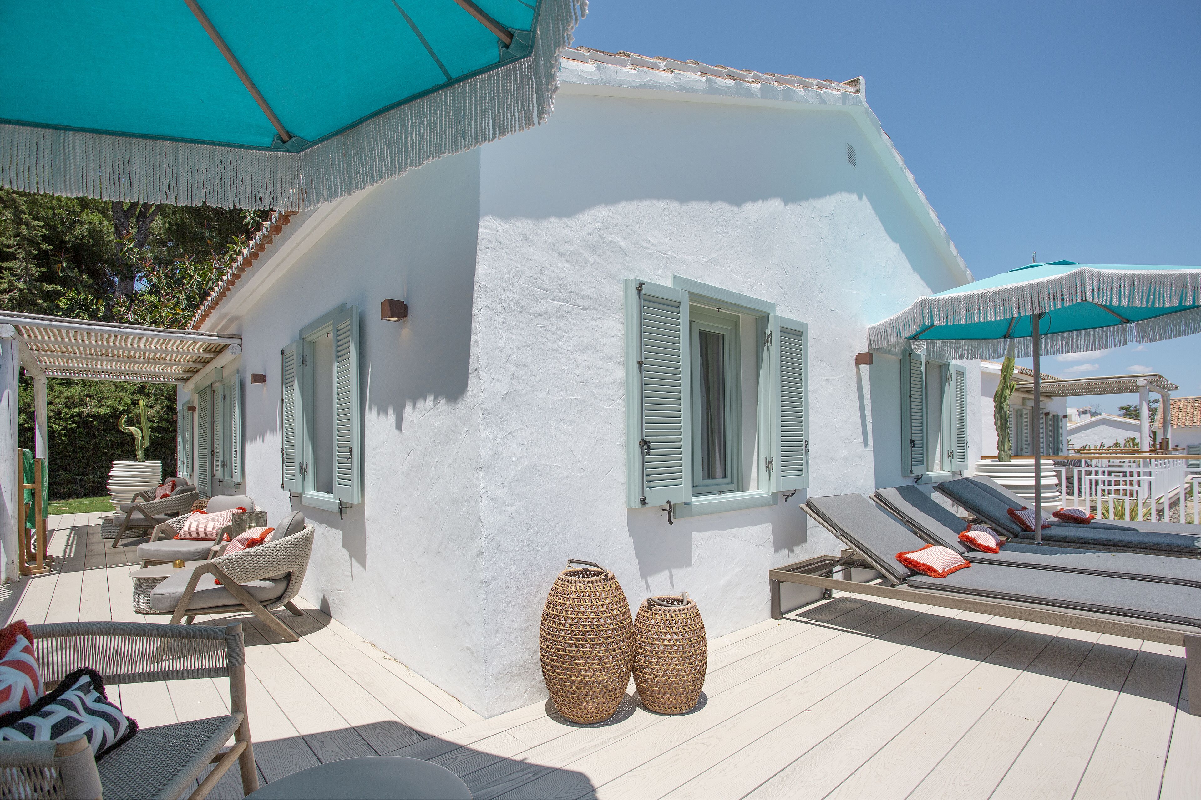 A white building with green shutters, outdoor seating with cushions, and two large woven baskets.