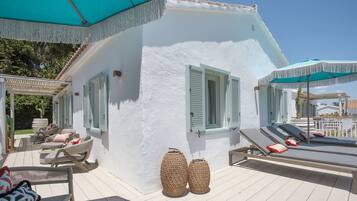 A white building with green shutters, outdoor seating with cushions, and two large woven baskets.