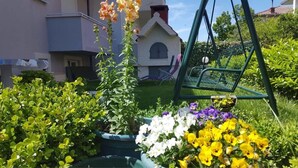 A garden with various plants and flowers, a swing set, and a building in the background. - Apartments Milic (Kastela)