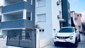 A modern multi-story residential building with balconies, a gated entrance, and a parked white car. - Apartments Milic (Kastela)