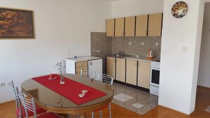 A compact kitchen with a dining area, featuring a round table with chairs, a small refrigerator, and a coffee machine. - Apartments Milic (Kastela)
