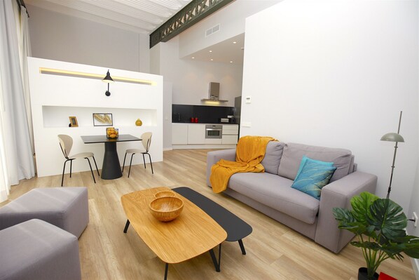 Una sala moderna con un sofá gris, una mesa de centro de madera y un comedor con una mesa y sillas blancas.