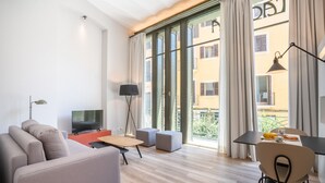 Un salon moderne avec un canapé, un téléviseur, une table et un balcon agrémenté de rideaux.