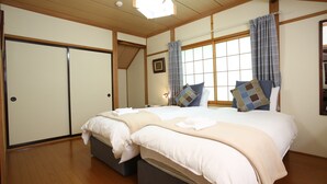 Una camera da letto in stile tradizionale giapponese, con due letti, pavimento in legno e una porta scorrevole.