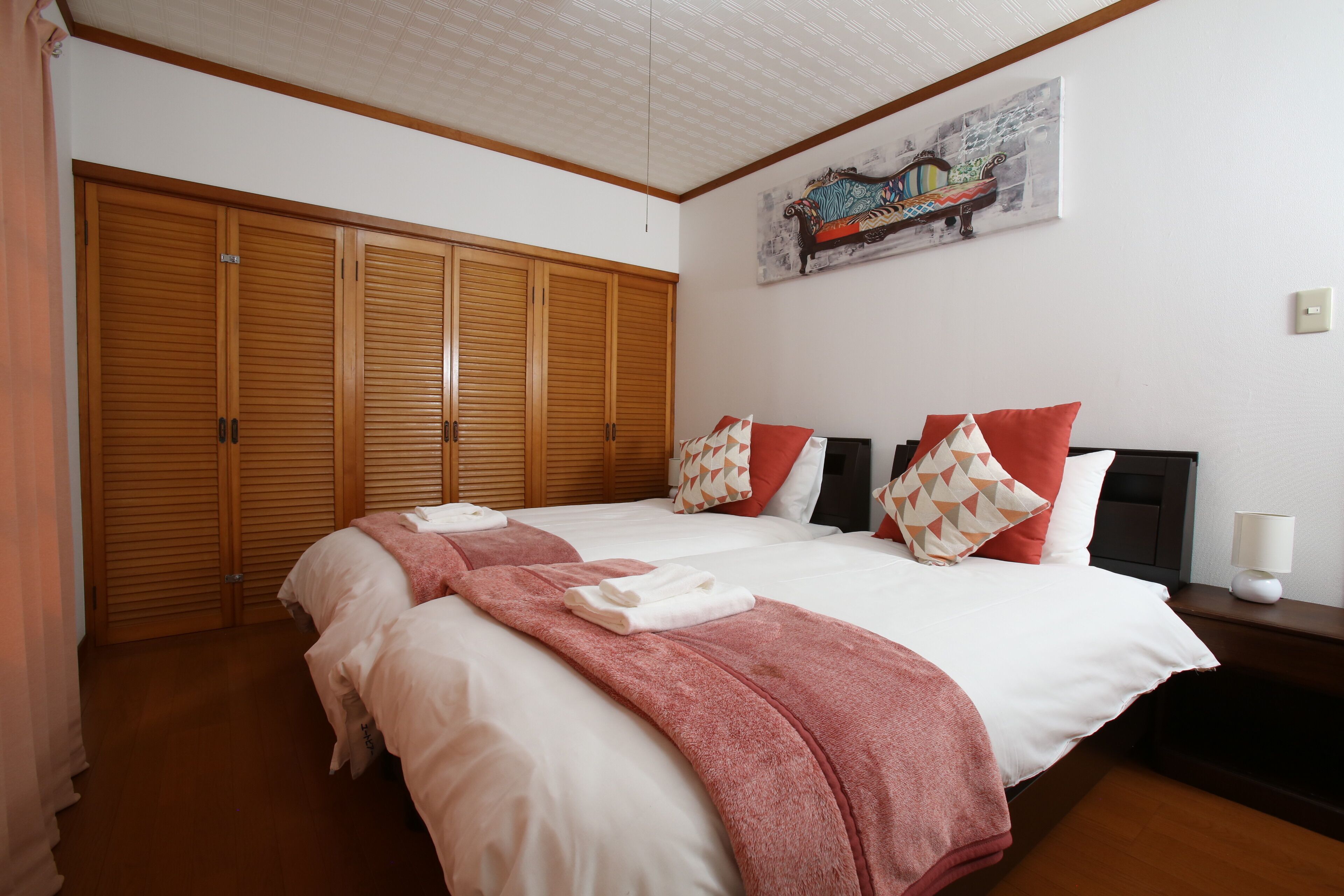 A hotel room with a large bed, a wardrobe, a painting on the wall, and a bedside table with a lamp.