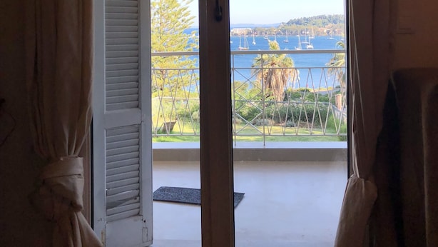 Ein Zimmer mit einer Schiebetür zu einem Balkon mit Blick auf das Meer und Boote.