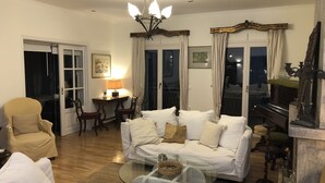 Ein Wohnzimmer mit einer Sofagarnitur, einem Glastisch, einem Klavier und einer Chandelier.