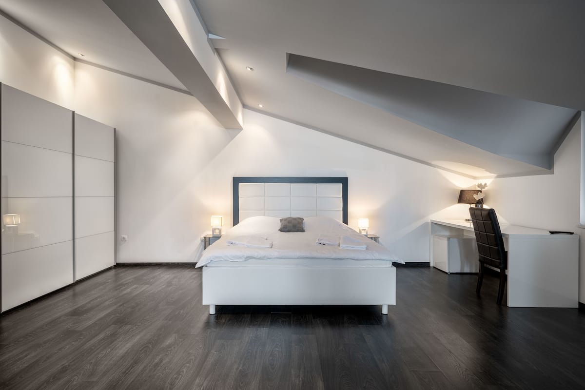 A modern bedroom with a sloped ceiling, a large bed, bedside tables, and a desk with a chair.