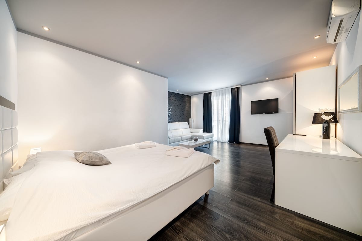 A modern hotel room with a large bed, a desk, a chair, a TV, and a bathroom with a shower and toilet.