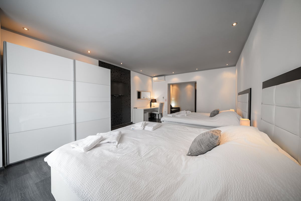 A modern hotel room with a large bed, a desk, and a wardrobe.
