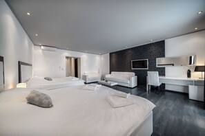Ein modernes Hotelzimmer mit einem großen Bett, zwei Sofas, einem Schreibtisch und einem Fernseher.